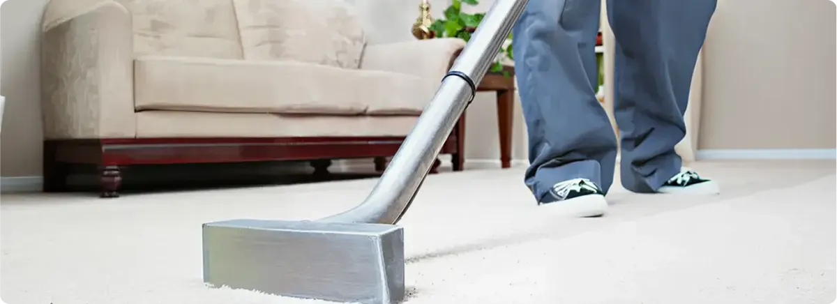 Carpet cleaning technician using a hot-water extraction wand on a light-colored carpet in a living room, Mobile, AL.